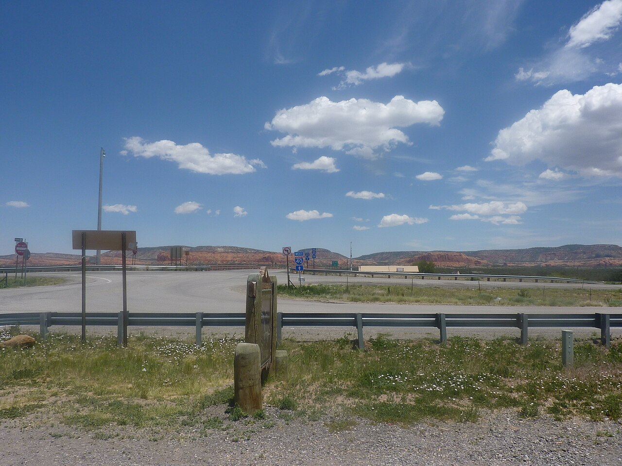 A scenic high-desert view at the Continental Divide near I-40 in New Mexico, looking out over grassland and red-rock mesas from the historic Old Route 66 marker.