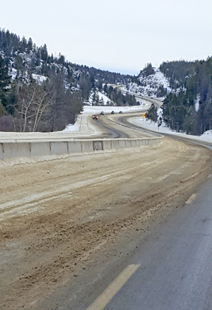 Interstate 90 winding over Homestake Pass in winter, with snow-dusted, pine-covered slopes flanking the highway as it crosses the Continental Divide.