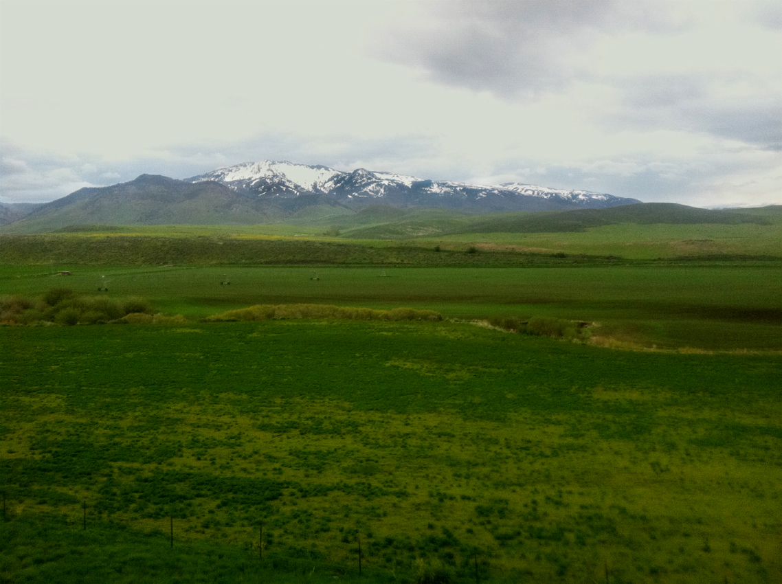 Snow-capped peaks of the Malad Range rise above the green valley near Malad Pass, the summit of I-15 in southeastern Idaho.